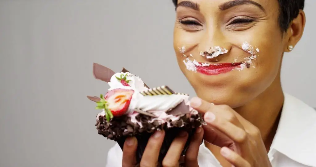 enjoy emotional eating picture of woman eating piece of cake and smiling with frosting on her nose