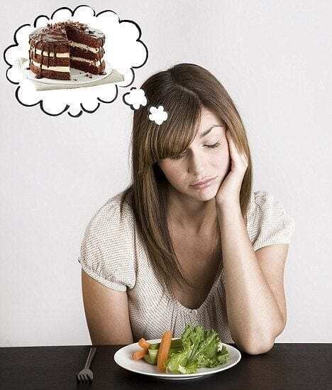 picture of woman experiencing a food craving for chocolate cake as she stares dismally at a piece of lettuce