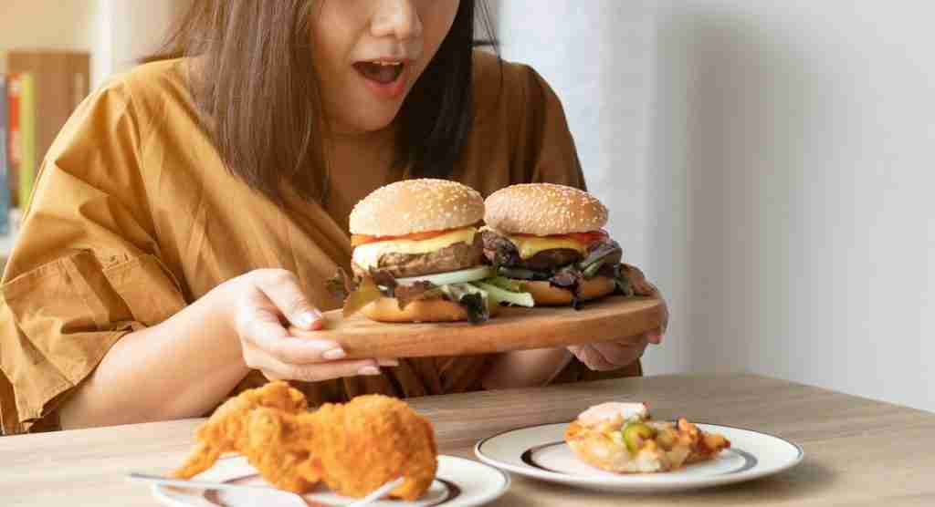 stress eating picture with woman holding burgers to talk about how to stop overeating